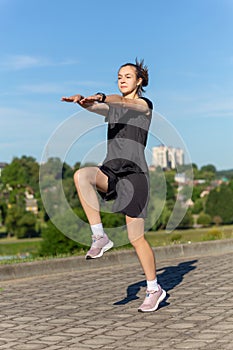 Young, fit and sporty girl in black clothes stretching after the workout in the urban city park