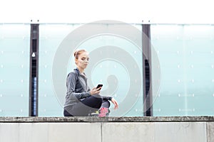 Young, fit and sporty girl sitting on a concrete border. Fitness, sport, urban jogging and healthy lifestyle concept.