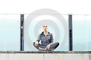 Young, fit and sporty girl sitting on a concrete border. Fitness, sport, urban jogging and healthy lifestyle concept.