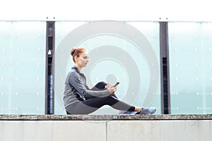 Young, fit and sporty woman sitting on a concrete border. Fitness, sport, urban jogging and healthy lifestyle concept.