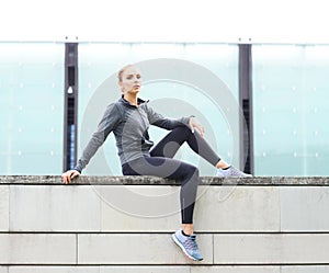 Young, fit and sporty woman sitting on a concrete border. Fitness, sport, urban jogging and healthy lifestyle concept.