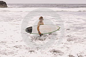 young fit surfer man with surfboard runs into ocean or sea with big waves for surfing. Concept of extreme sport, fitness