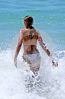 Young, fit, tanned woman walking through a wave out to sea.