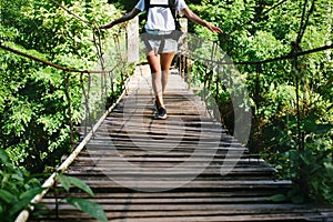 Young fit woman with backpack traveling across hanging bridge in tropical forest