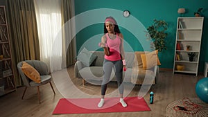 Young fit woman doing bicep exercises with dumbbells at home. An African American woman lifts dumbbells through pain and