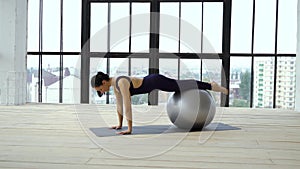 Young fit woman doing exercises with fitness ball in studio