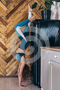 Young fit woman doing handstand exercise in kitchen resists the temptation to eat.