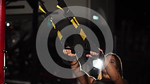 Young fit woman doing pull-ups on gymnastic rings. Muscular young female athlete exercising with rings at gym.