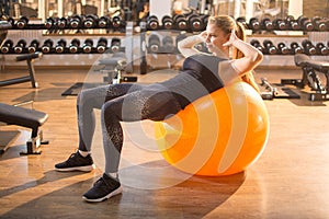 Young fit woman doing sit-ups on a fitness ball in gym.
