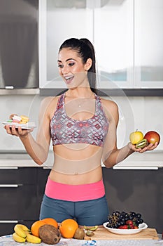 Young fit woman in the kitchen holding fruits and macarons