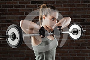 Young fit woman lifting dumbbells on brick background