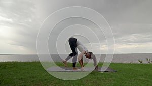 Young fit woman practice yoga on coast near the lake or sea. Woman doing Balancing Standing Splits and then Standing