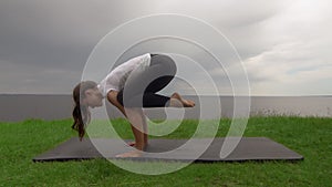 Young fit woman practice yoga on coast near the lake or sea. Woman doing Crane Bakasana pose