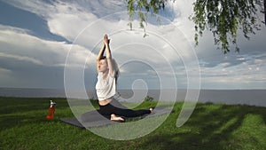 Young fit woman practice yoga on coast near the lake or sea. Woman doing Half Pigeon Pose
