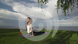 Young fit woman practice yoga on coast near the lake or sea. Woman doing High Cobra Bhujangasana Pose