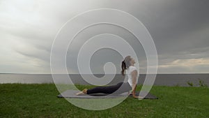 Young fit woman practice yoga on coast near the lake or sea. Woman doing High Cobra Pose