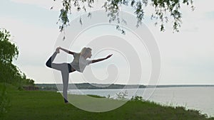 Young fit woman practice yoga on coast near the lake or sea. Woman doing Lord of the Dance Pose