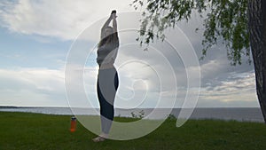 Young fit woman practice yoga on coast near the lake or sea. Woman doing Mountain Arms Up Pose