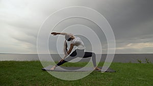 Young fit woman practice yoga on coast near the lake or sea. Woman doing Reverse Warrior Pose