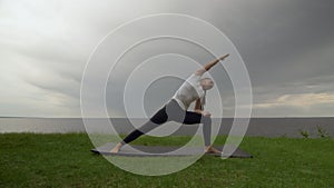 Young fit woman practice yoga on coast near the lake or sea. Woman doing Revolved Warrior with Arms Extended Pose