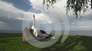 Young fit woman practice yoga on coast near the lake or sea. Woman doing Side Forearm Plank Pose