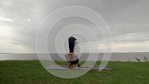 Young fit woman practice yoga on coast near the lake or sea. Woman doing Standing Forward Bend Pose