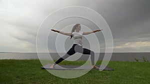 Young fit woman practice yoga on coast near the lake or sea. Woman doing Warrior II Pose