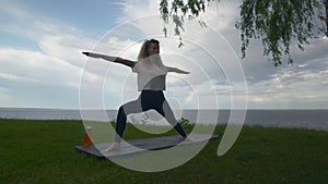 Young fit woman practice yoga on coast near the lake or sea. Woman doing Warrior one and two Poses