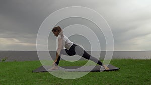 Young fit woman practice yoga on coast near the lake or sea. Woman doing Warrior two then Upward-Facing Dog Poses