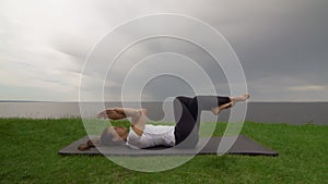 Young fit woman practice yoga on coast near the lake or sea. Woman lays on back with curled legs and arms