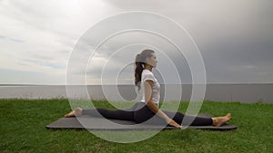 Young fit woman practice yoga on coast near the lake or sea. Woman sitting in Front Splits Hanumanasana pose