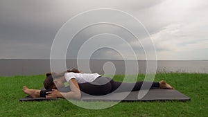 Young fit woman practice yoga on coast near the lake or sea. Woman sitting in Front Splits Hanumanasana pose