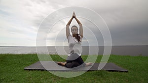 Young fit woman practice yoga on coast near the lake or sea. Woman sitting in Knee Pile pose and meditating