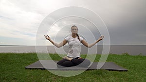 Young fit woman practice yoga on coast near the lake or sea. Woman sitting in Knee Pile pose and meditating