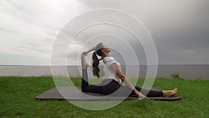 Young fit woman practice yoga on coast near the lake or sea. Woman sitting in One Legged King Pigeon - Mermaid pose