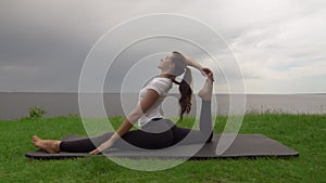 Young fit woman practice yoga on coast near the lake or sea. Woman sitting in One Legged King Pigeon - Mermaid pose
