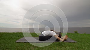 Young fit woman practice yoga on coast near the lake or sea. Woman sitting in Seated Forward Bend pose