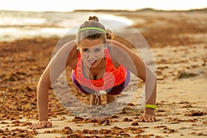 Young fit woman in sports gear on seashore doing pushups