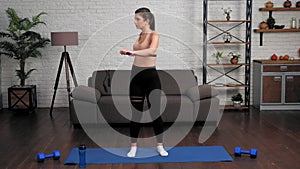 Young fit woman in sportswear doing warm-up before workout on yoga mat at home