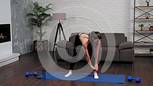Young fit woman in sportswear doing warm-up before workout on yoga mat at home