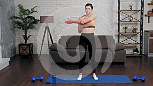 Young fit woman in sportswear doing warm-up before workout on yoga mat at home