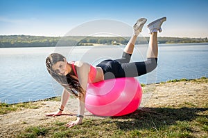 Young fit woman in sportswear during fitness time and exercising with ball at the lake. Healthy lifestyle