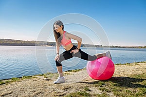 Young fit woman in sportswear during fitness time and exercising with ball at the lake. Healthy lifestyle