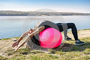 Young fit woman in sportswear during fitness time and exercising with ball at the lake. Healthy lifestyle