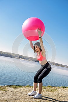 Young fit woman in sportswear during fitness time and exercising with ball at the lake. Healthy lifestyle