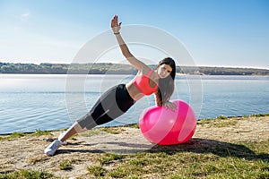 Young fit woman in sportswear during fitness time and exercising with ball at the lake. Healthy lifestyle