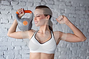 Young fit woman in sportswear holding kettlebell on shoulder