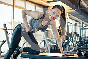 Young fit woman in sportswear working out with weights over fitness bench in gym.
