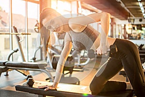 Young fit woman in sportswear working out with weights over fitness bench in gym.