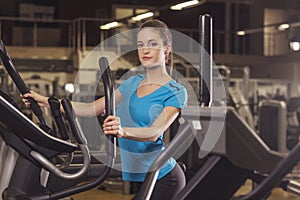 Young fit woman using an elliptic trainer in a fitness center, back shot. Portrait of fitness girl in the gym.